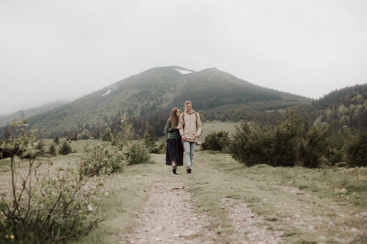 A couple enjoying a peaceful walk through lush green mountains on a cloudy day.