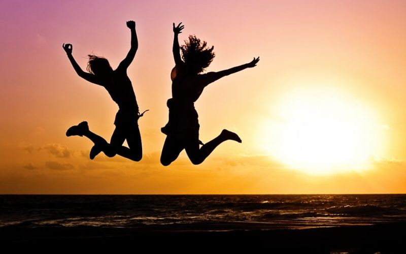 Silhouettes of two people joyfully jumping on a beach during a vibrant sunset.